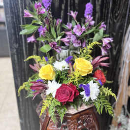 Mixed bouquet with yellow and red roses, white daisies, and purple flowers in a vase