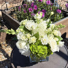 White floral arrangement in a square glass vase with green blooms