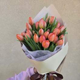 Bouquet of pink-orange tulips wrapped in cream paper with a ribbon