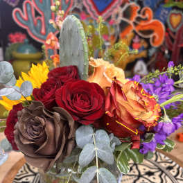 Mixed bouquet of roses, sunflowers, and purple flowers in a glass vase