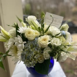 White roses, lilies, daisies, and blue hydrangea in a cobalt vase