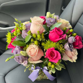 Bouquet of pink and lavender roses in a glass vase with a purple ribbon