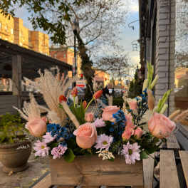 Pastel floral arrangement in a wooden box with roses, tulips, and daisies
