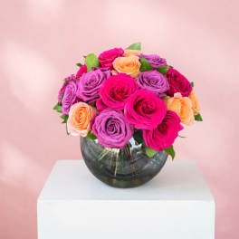Bouquet of pink, purple, and peach roses in a round glass vase
