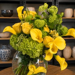 Yellow calla lilies and roses arranged with green hydrangeas in a glass vase