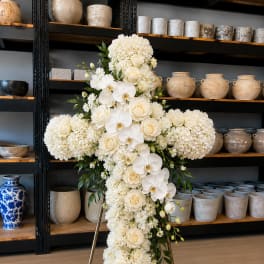 White floral cross arrangement on a stand with roses and orchids