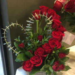 Red roses arranged in a square gray container with greenery