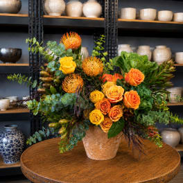 Orange and yellow roses in a peach vase with green foliage