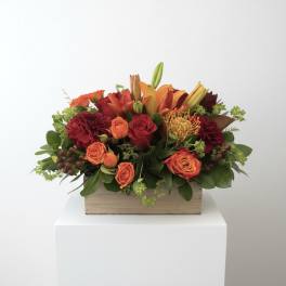 Orange and red floral arrangement in a wooden box