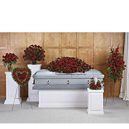 Funeral casket surrounded by red rose sprays and a heart wreath