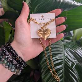 Hand holding a gold heart pendant necklace on a card