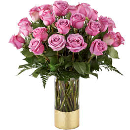 Pink roses arranged in a tall glass vase with a gold base
