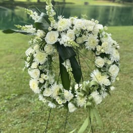 White floral wreath on a stand with green ribbon accents