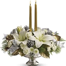 White floral centerpiece with two gold taper candles in a silver pedestal bowl
