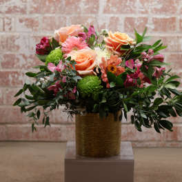 Mixed bouquet of peach roses, pink daisies, and green mums in a gold vase
