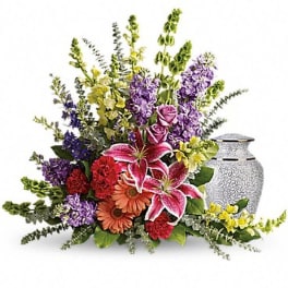 Colorful floral arrangement with lilies, roses, and gerbera daisies beside a silver urn