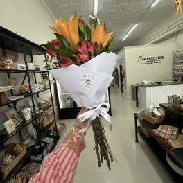 Handheld bouquet of orange lilies and pink flowers wrapped in white paper