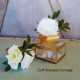 Two white floral cuff corsages with gold bracelet bands and greenery