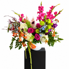 Bright mixed flower arrangement in a white vase on a black pedestal