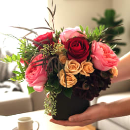 Handheld bouquet of pink and red roses in a black vase