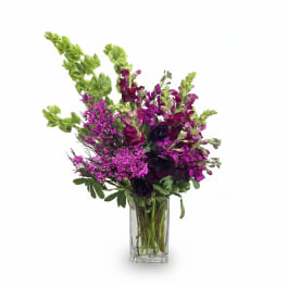 Tall arrangement of purple and green flowers with bells of Ireland and snapdragons in a clear glass vase