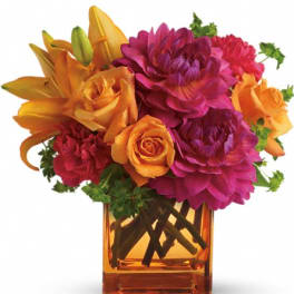 Orange and magenta flowers arranged in a square glass vase