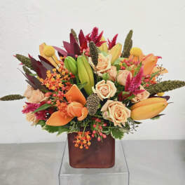Mixed bouquet of peach roses, orange lilies, and pink accents in a square vase