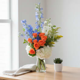 Bouquet of orange roses, blue delphinium, and white hydrangeas in a glass vase