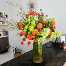 Orange roses and green blooms in a tall glass vase
