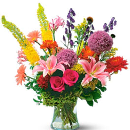 Colorful mixed bouquet in a clear glass vase with lilies, roses, and daisies