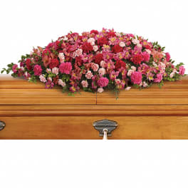 Pink and red floral casket spray on a wooden casket