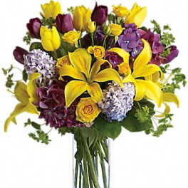 Bouquet of yellow lilies, purple flowers, and roses in a clear glass vase