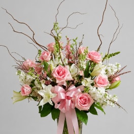 Pink roses and white lilies in a glass vase with a pink ribbon