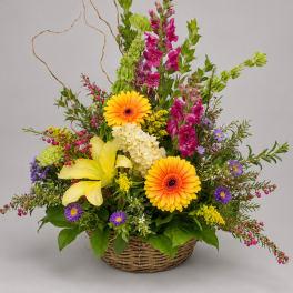 Basket arrangement with yellow lilies, orange gerberas, and purple flowers