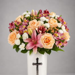 Peach roses and pink lilies in a white vase with a cross