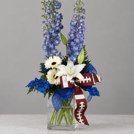 Tall blue and white floral arrangement in a clear glass vase with football ribbon