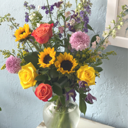 Mixed bouquet of sunflowers, roses, and purple flowers in a glass vase