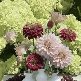 Bouquets of pink and white flowers in small white vases with grapes and bread
