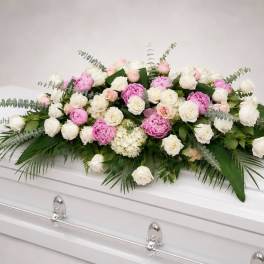 Pink and white rose casket spray with greenery on a white coffin