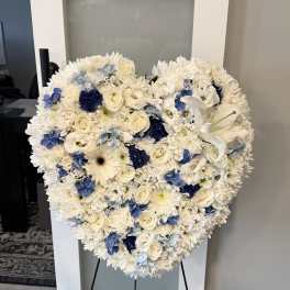 Heart-shaped floral spray with white flowers and blue accents on a stand