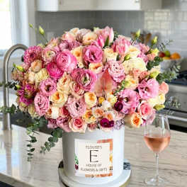 Large pink and cream floral arrangement in a white hat box beside a wine glass