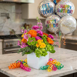 Bright mixed flower arrangement in a white cube vase with birthday balloons