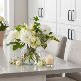 White floral arrangement in a clear glass vase on a table beside a candle