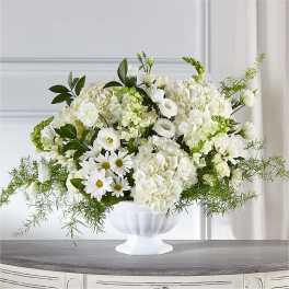 White floral arrangement in a white pedestal vase with green accents
