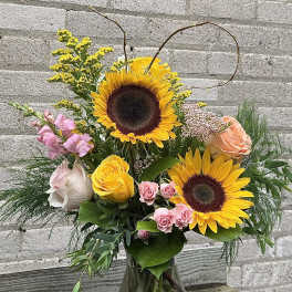 Sunflower and rose bouquet in a glass vase with curly branches