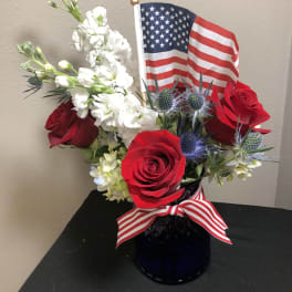 Red roses and white flowers arranged in a vase with an American flag
