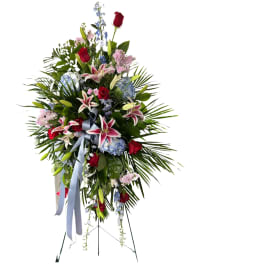 Tall standing floral spray with red roses, lilies, and blue flowers on an easel