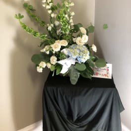 Tall floral arrangement with white blooms, blue hydrangea, and a white ribbon