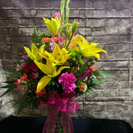 Tall mixed bouquet of yellow lilies and pink flowers in a glass vase