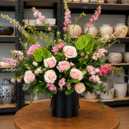 Pink roses and mixed blooms arranged in a black hatbox-style container
